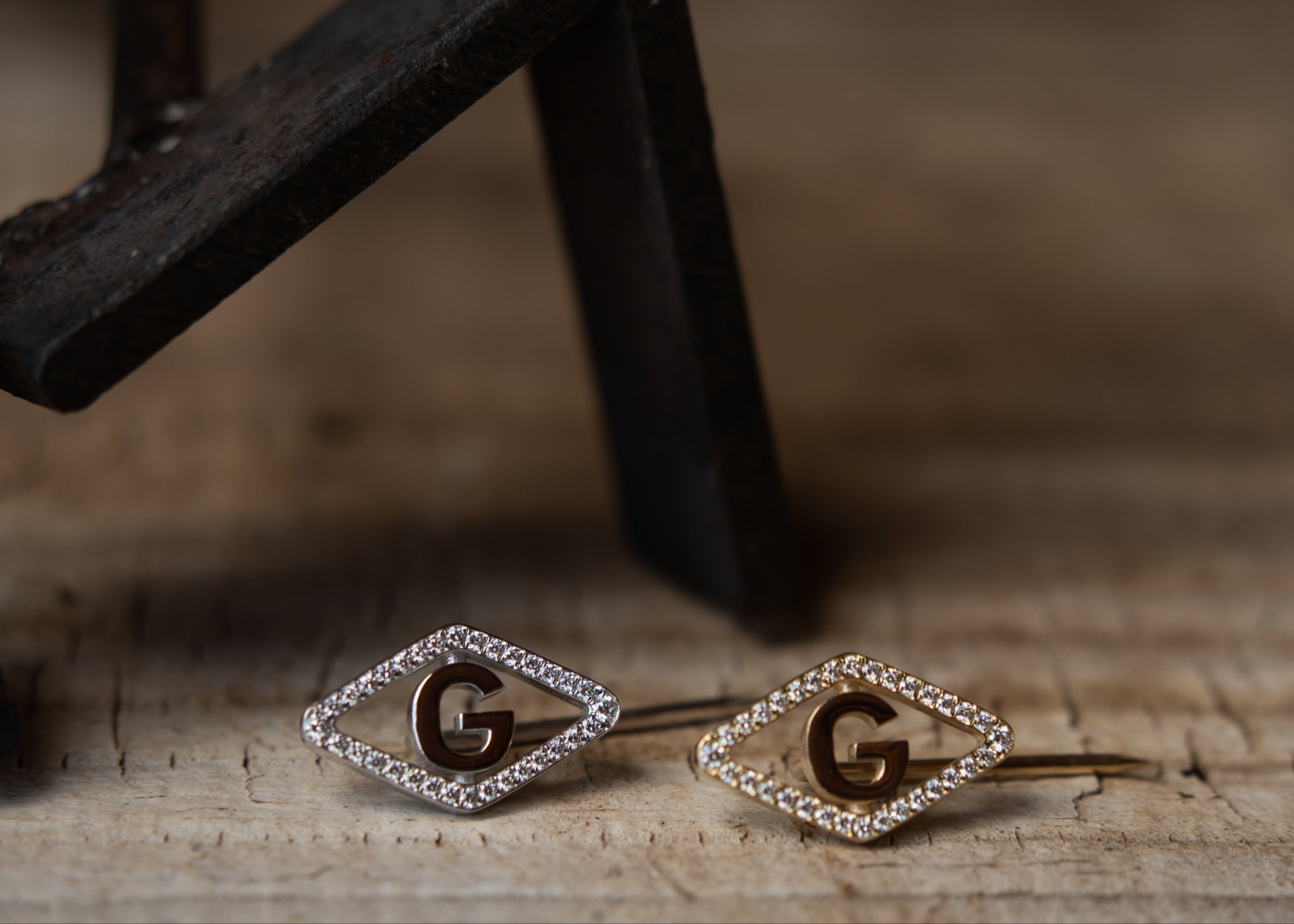 Gold earrings with 'G' initials on a wooden surface