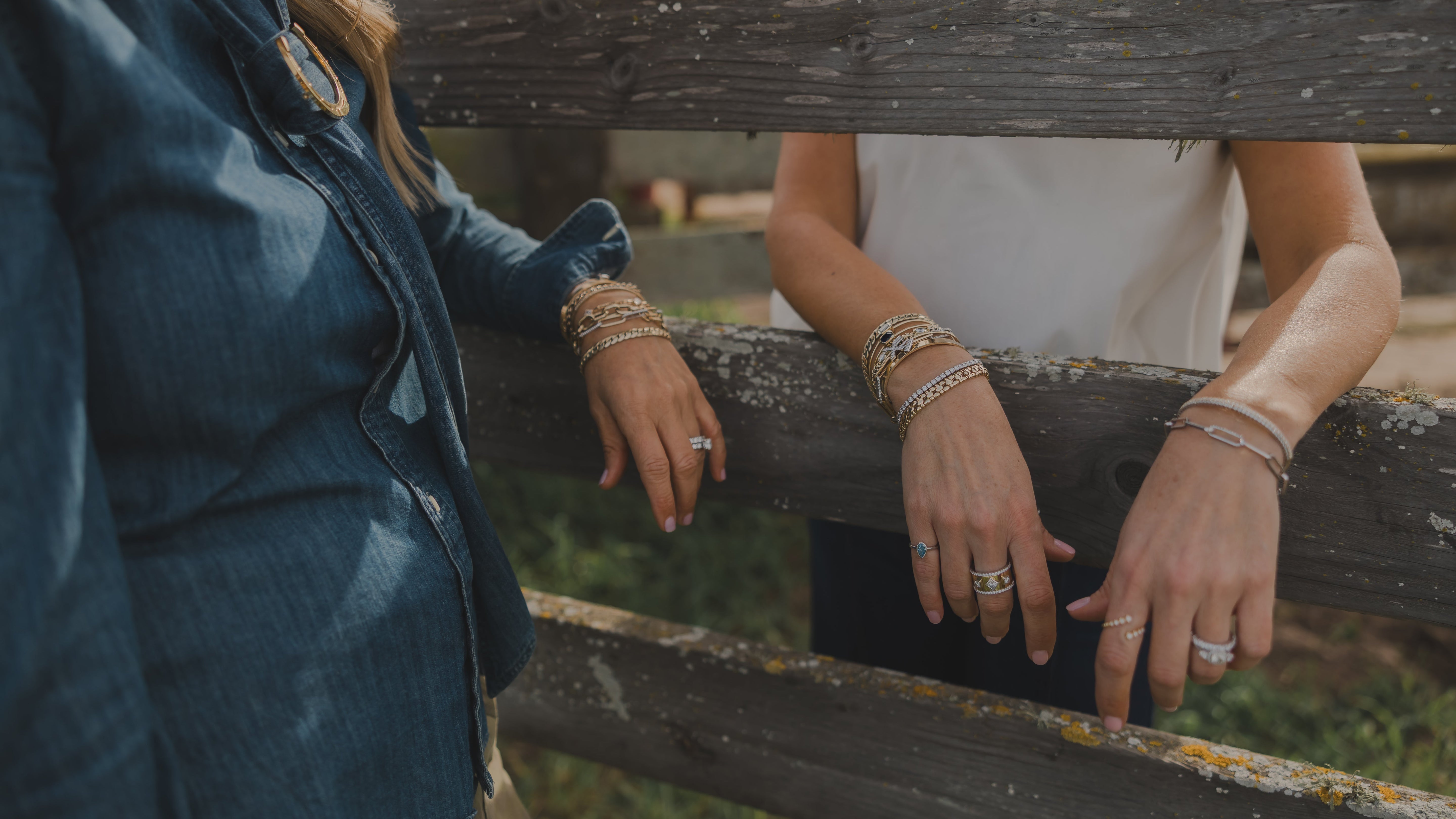 Two people wearing jewelry, including rings and bracelets, standing behind a wooden fence.