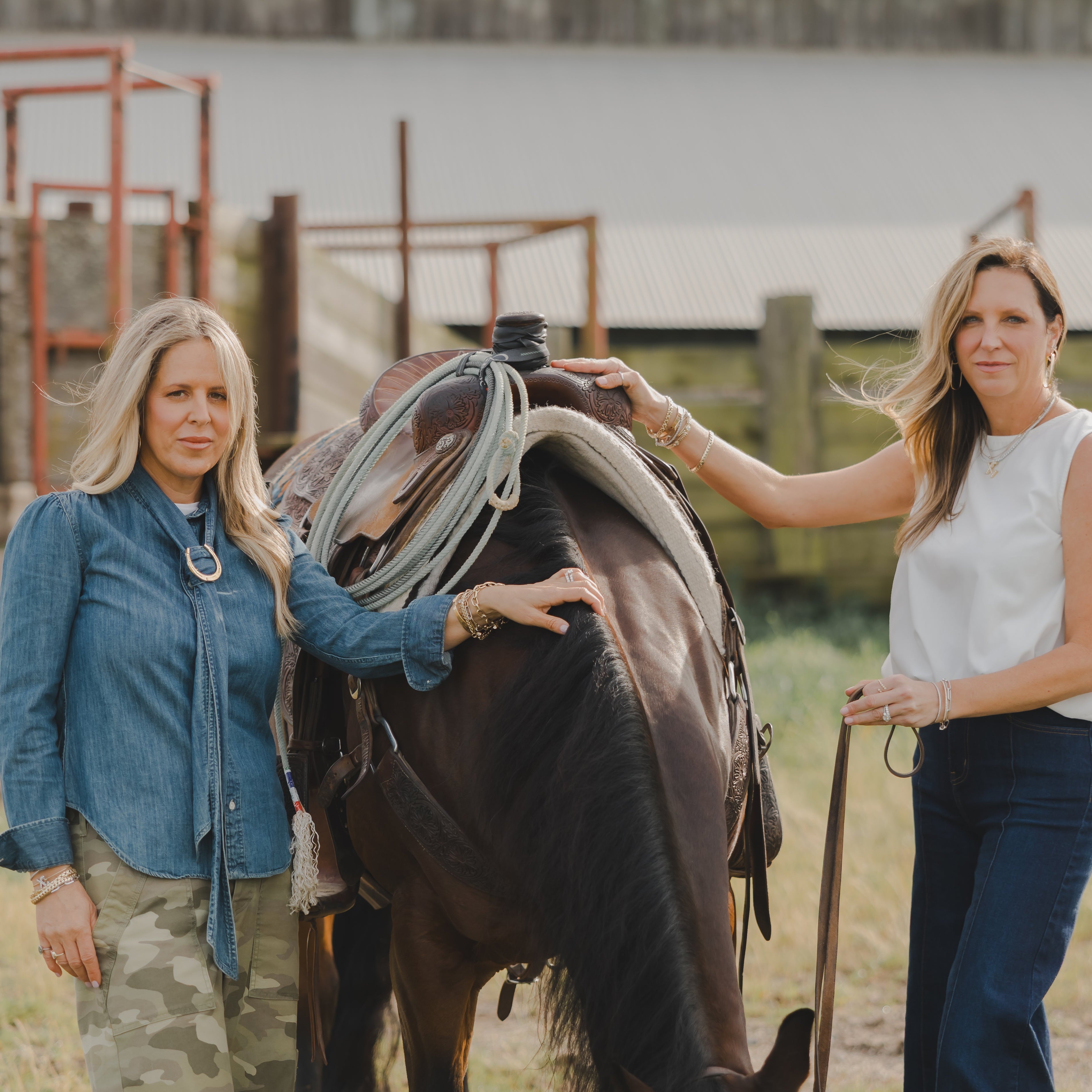 Two women standing with a horse in an outdoor setting near a body of water.