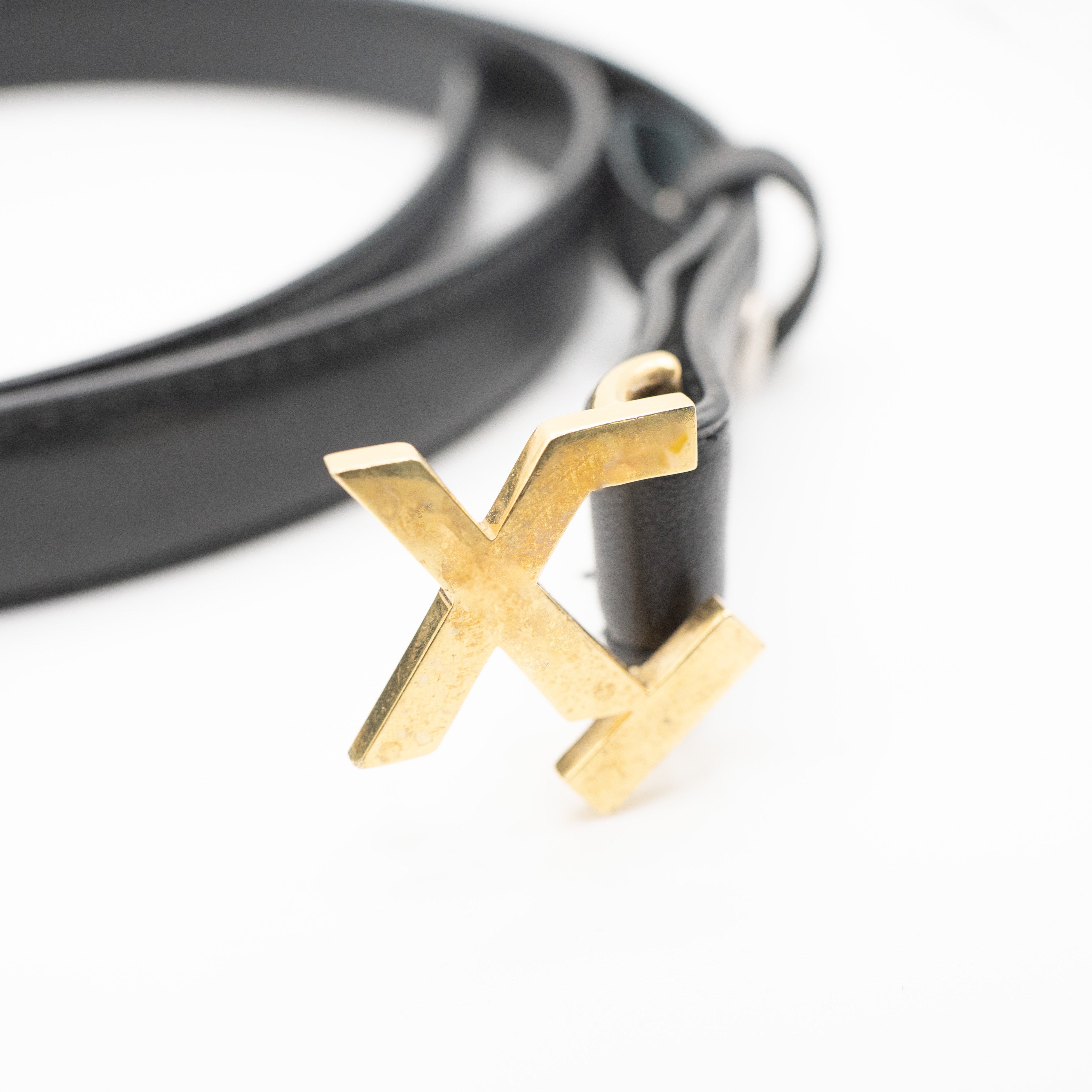 Black belt with a gold 'X' buckle on a white background