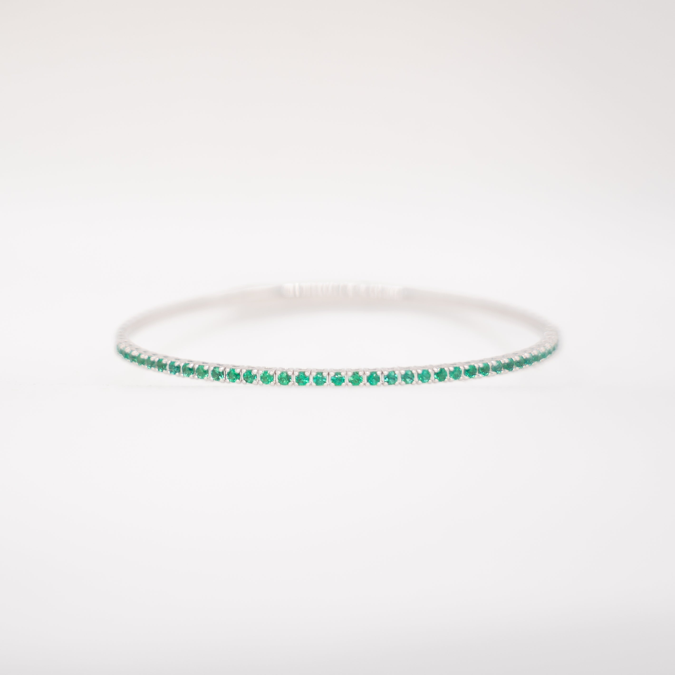 Thin silver bracelet with green gemstones on a white background