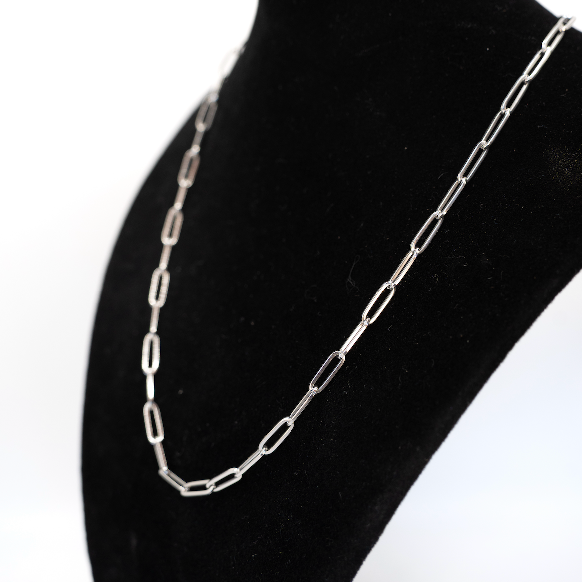 Silver chain necklace on a black mannequin bust against a white background